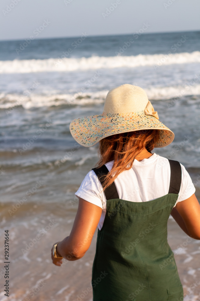 Rear view of a young African lady in a hat facing the ocean