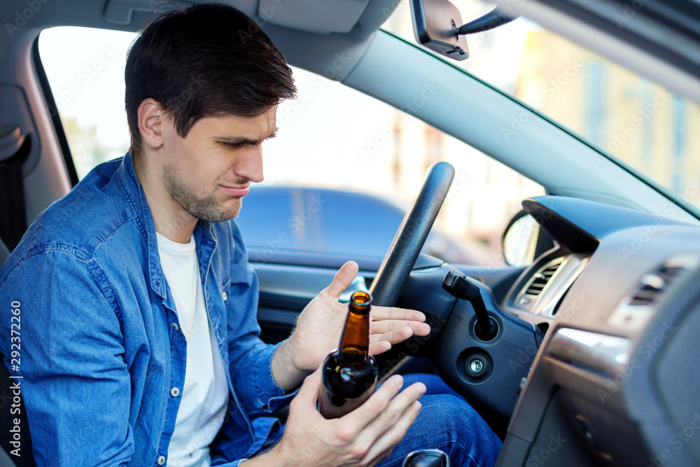 Young brunette man is drinking beer behind steering wheel of car. Drunk ...