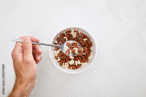 cropped image of man taking cereal with spoon from bowl on marble surface