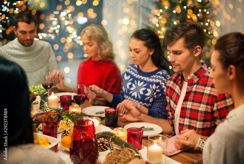 holidays and celebration concept - friends holding hands and praying while having christmas dinner at home