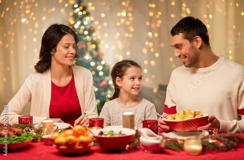 holidays, family and celebration concept - happy mother, father and little daughter having christmas dinner at home