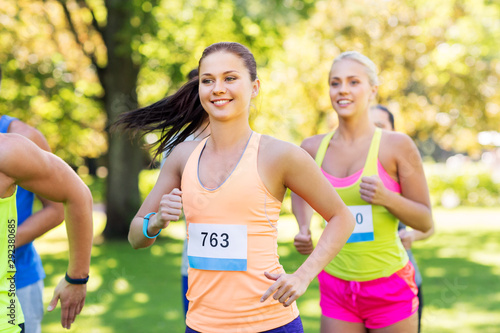 fitness, sport, race and healthy lifestyle concept - group of happy people or sportsmen running marathon with badge numbers at summer park