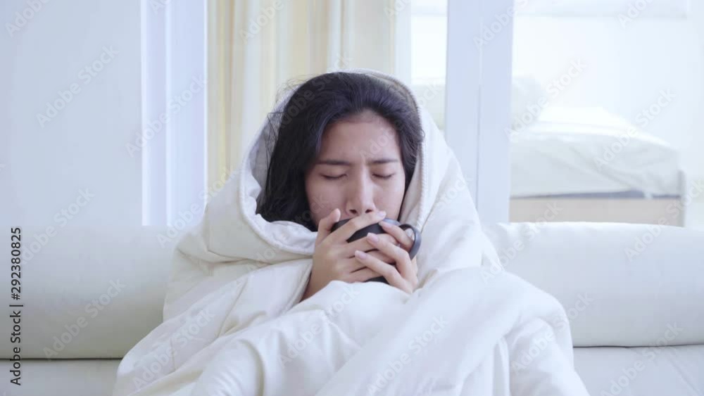 Sick woman holding and blowing a cup of hot drink while covering her body with a blanket on the sofa in the living room at home. Shot in 4k resolution Sick woman holding and blowing a cup of hot drink while covering her body with a blanket on the sofa in the living room at home. Shot in 4k resolution