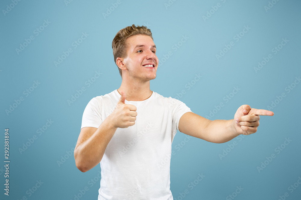 Caucasian young man's half-length portrait on blue studio background. Beautiful male model in shirt. Concept of human emotions, facial expression, sales, ad. Pointing at side, smiling. Caucasian young man's half-length portrait on blue studio background. Beautiful male model in shirt. Concept of human emotions, facial expression, sales, ad. Pointing at side, smiling.