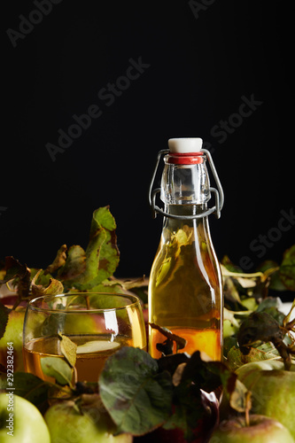 bottle and glass of fresh cider near ripe apples isolated on black
