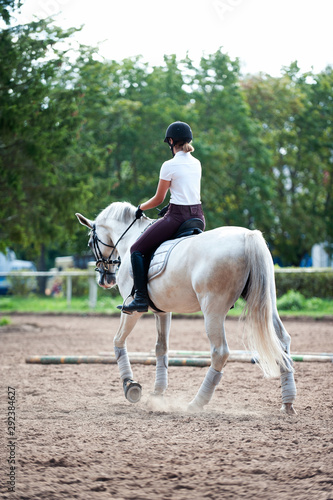 Young teenage girl equestrian practicing horseback riding on manege