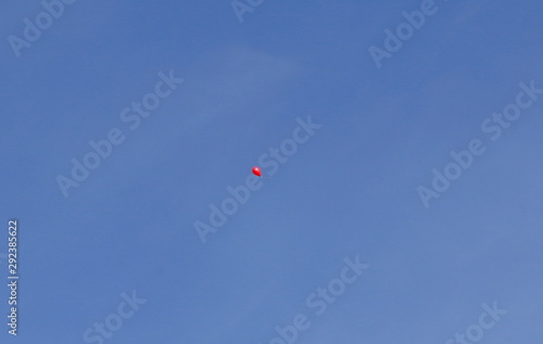 A red balloon rises into the immense blue sky
