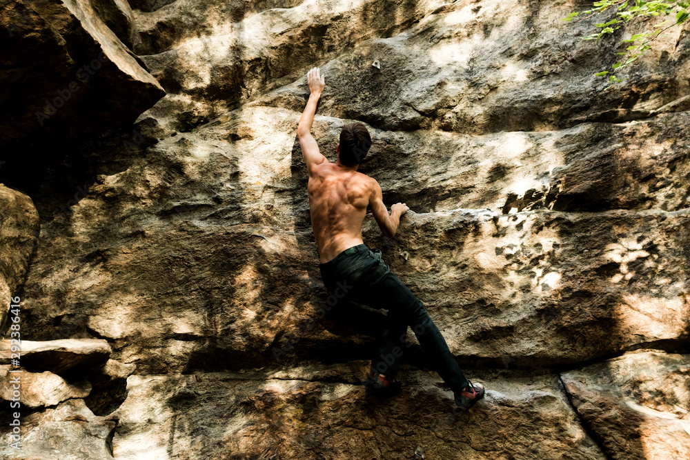 Rock climber climbs bouldering on a cliff on forest. Low angle of strong rock climbing man hanging free on rock with sunflare Rock climber climbs bouldering on a cliff on forest. Low angle of strong rock climbing man hanging free on rock with sunflare