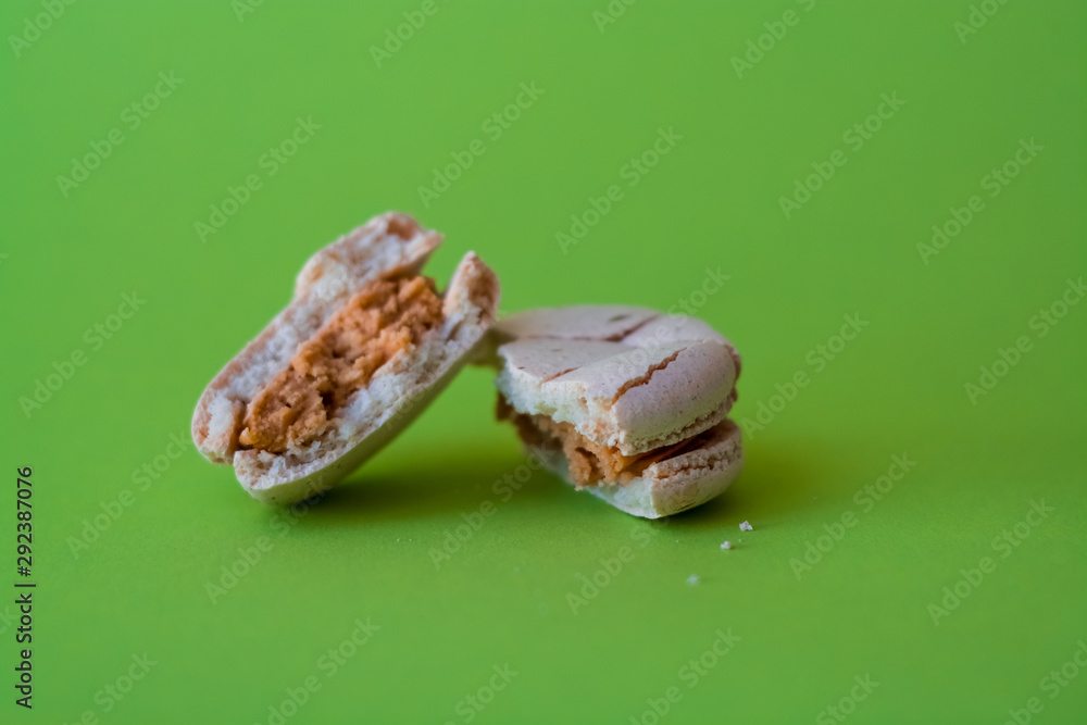 One broken macaron tastefully salted caramel on one-ton green background. French dessert. Sweets. One broken macaron tastefully salted caramel on one-ton green background. French dessert. Sweets.
