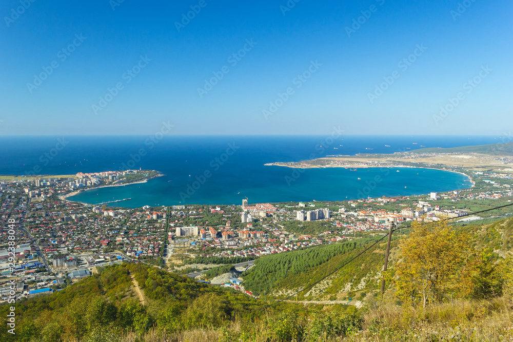Scenic view of Gelendzhik city and sea bay. Sunny day. Trees on hills on foreground. Photo of popular resort from hill of caucasian mountains.