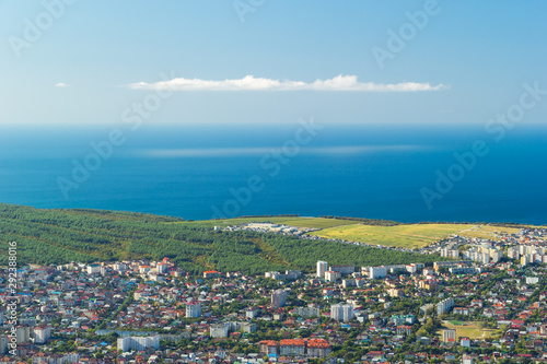 Scenic view of Black sea coastline and cityscape of Gelendzhik resort in Russia. Green forest areas, grass fields, residential houses.