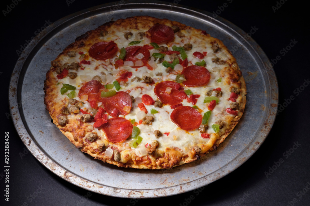 Whole unsliced hot pizza on round pizza pan with pizza cutter on dark background