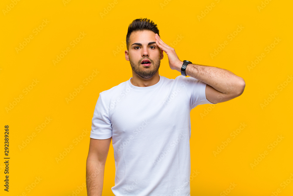 young hispanic man looking happy, astonished and surprised, smiling and realizing amazing and incredible good news against orange wall - obrazy, fototapety, plakaty 