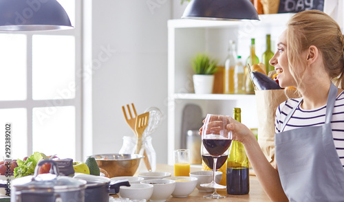 Beautiful woman in kitchen is drinking red wine