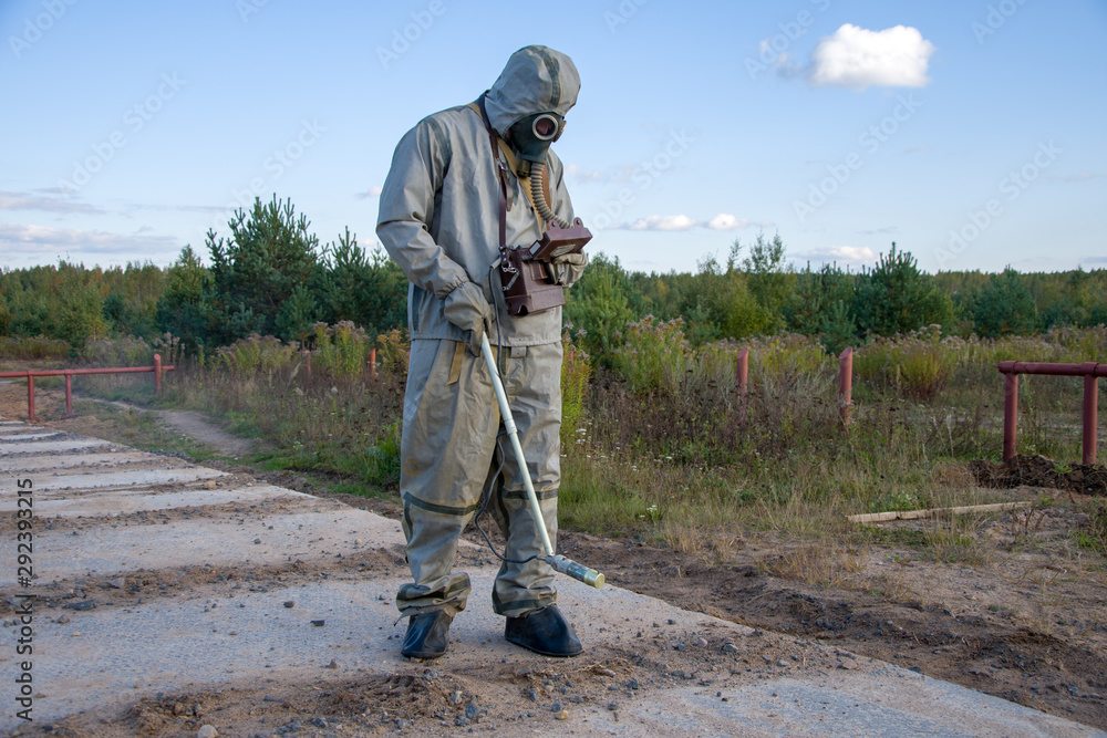 Chemist-dosimetrist measures the radiation of the concrete pavement of the road on the background of the forest and clouds