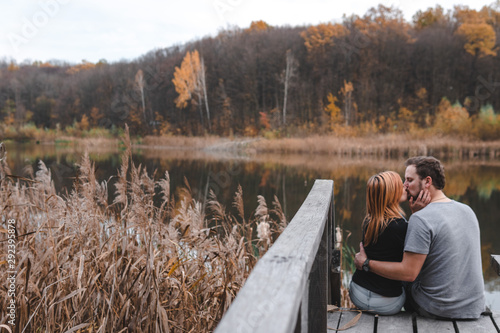 A couple on the old wooden bridge at a lake on autumn day. Forest on background. Happy togather, copy space for text. romantic moment, relationship. travel, hiking, outdoor. kiss. selective focus