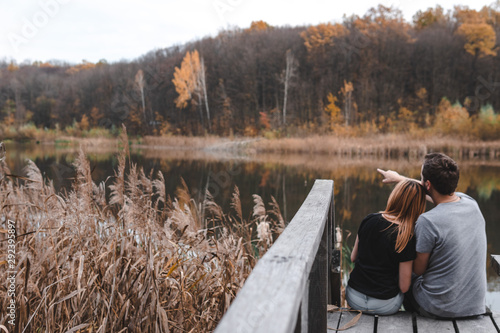 A couple on the old wooden bridge at a lake on autumn day in park. Forest on background. Selective focus, copy space for text. romantic moment, relationship. travel, hiking, outdoor. comfort