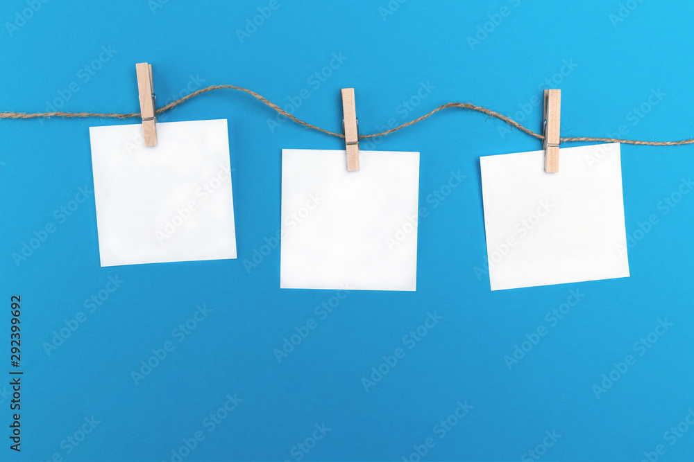 Three empty little sheets of paper hold by wooden clothespins on a string. Creative concept on a blue background and free copy space for the text Three empty little sheets of paper hold by wooden clothespins on a string. Creative concept on a blue background and free copy space for the text