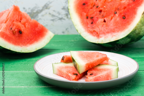 Ready-to-eat sliced watermelon on a plate and uncut watermelon on a green wooden table
