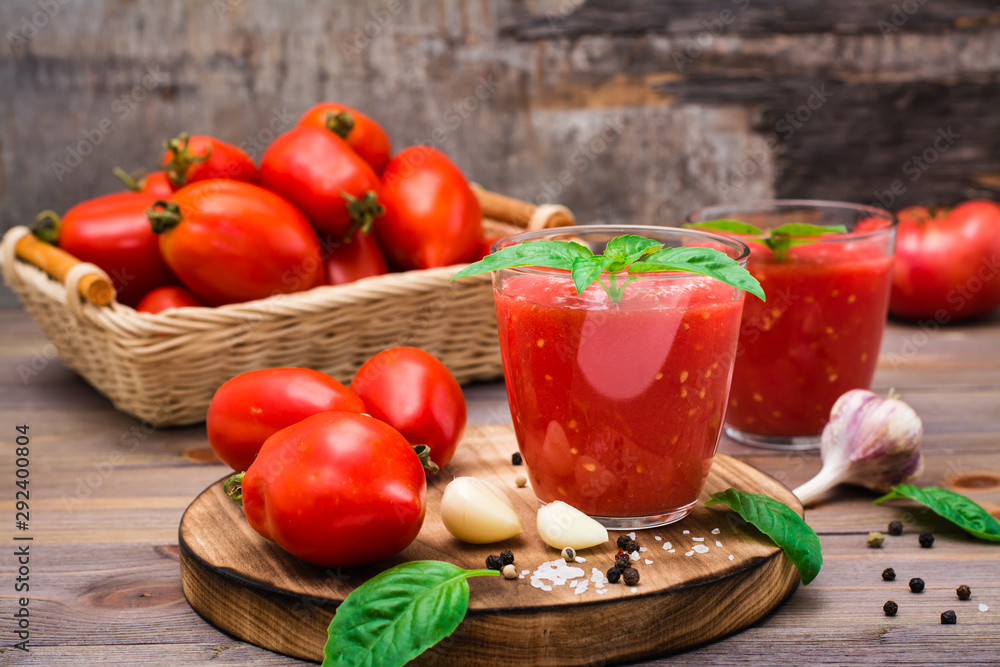 Ready-to-eat fresh tomato juice with basil leaves in glasses and tomatoes on a wooden table Ready-to-eat fresh tomato juice with basil leaves in glasses and tomatoes on a wooden table