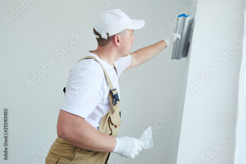 Painter with putty knife. Plasterer smoothing wall surface at home renewal photo