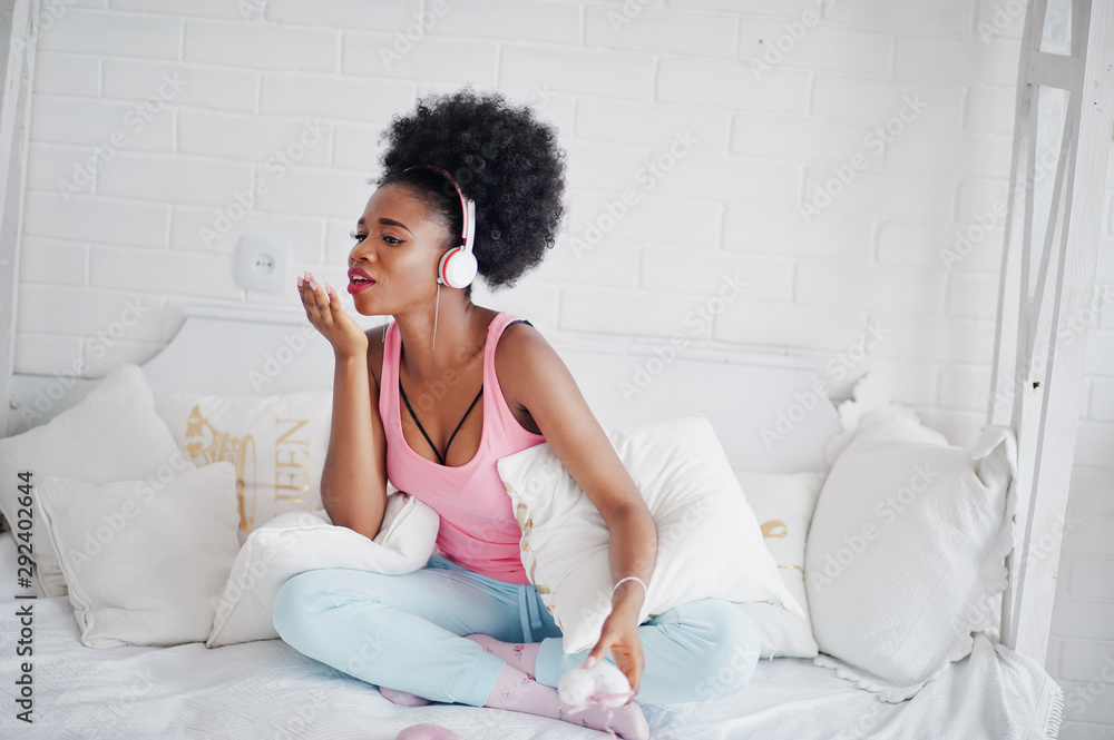 Young african american woman sitting in bed and listen music on earphones. Young african american woman sitting in bed and listen music on earphones.