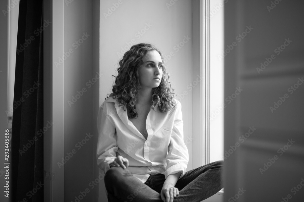 Beautiful young sad girl is sitting by the window Beautiful young sad girl is sitting by the window