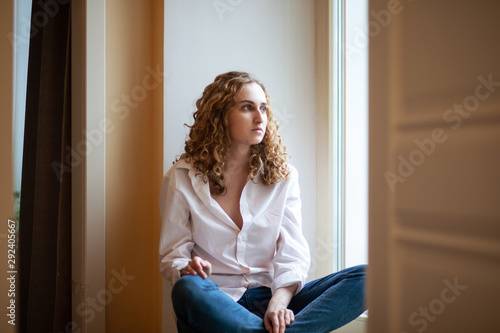 Beautiful young sad girl is sitting by the window