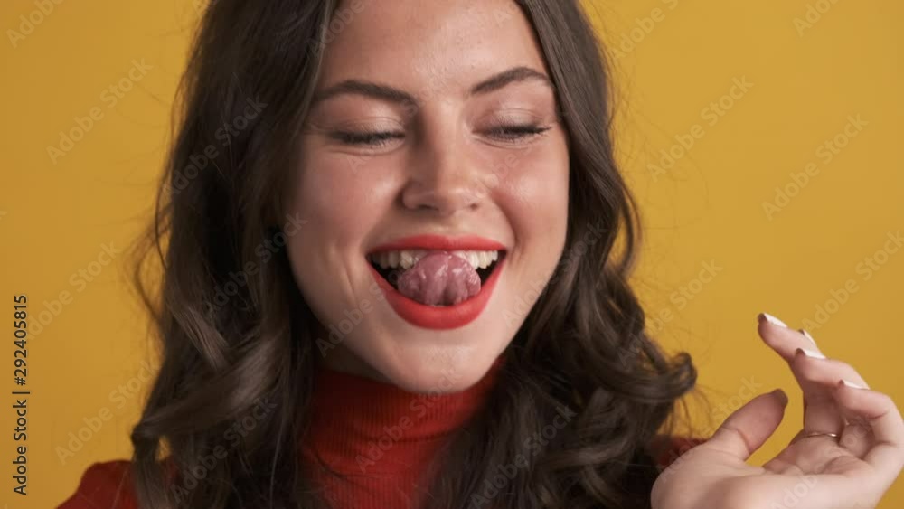 Portrait of attractive brunette girl happily licking teeth on camera over yellow background Portrait of attractive brunette girl happily licking teeth on camera over yellow background