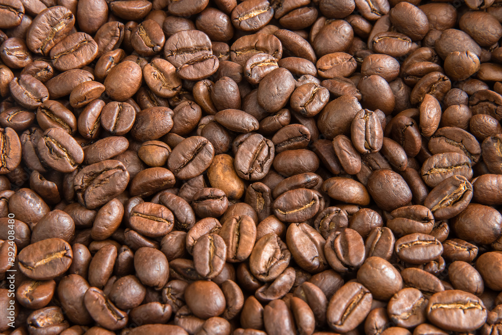 Naklejka premium Roasted coffee beans texture with a small bokeh. Brown coffee beans close-up photo with copy space