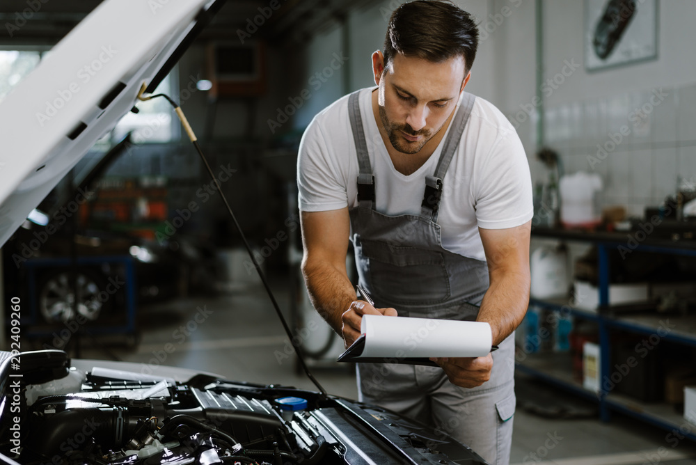 Young auto mechanic working on reports in a workshop Young auto mechanic working on reports in a workshop