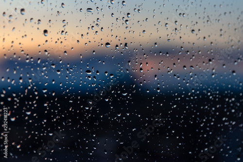Texture of water drops after rain on glass with sunset outside the window. Blurred sun and sky, beautiful dusk, rainy weather