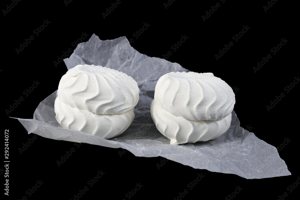 Obraz premium Two white marshmallows (zephyr) sprinkled with powdered sugar on a piece of baking paper isolated on black