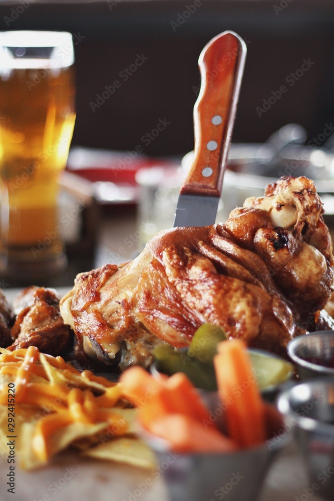 Pork knuckle with carrot, cucumber, sauce and beer on the background.