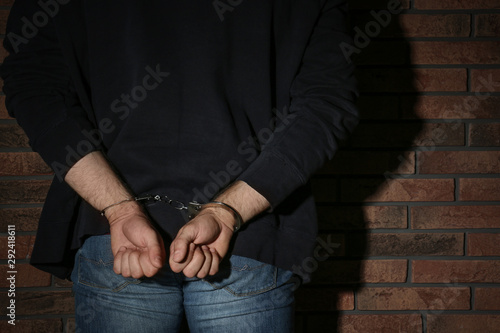 Male criminal in handcuffs near brick wall, closeup