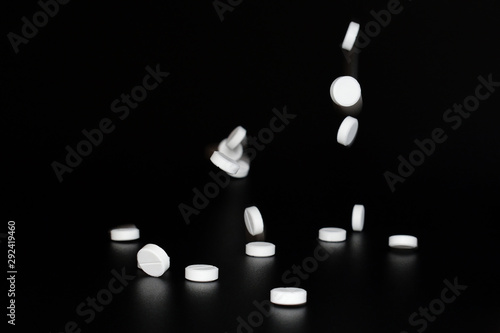 White pills falling on black background. Copy space. Tablets in the air