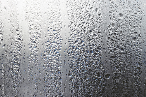 Steamy window background. Drops of condensate on the glass with reflections of naked trees