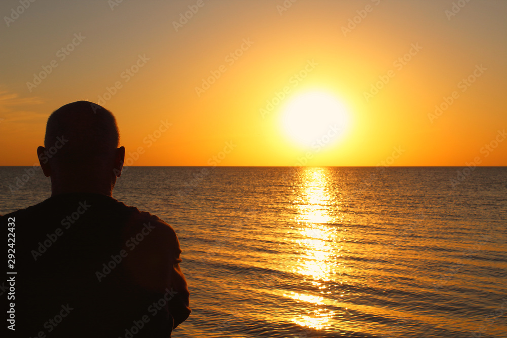 An adult man sits on the seashore and looks at the sunset. Background. Scenery.