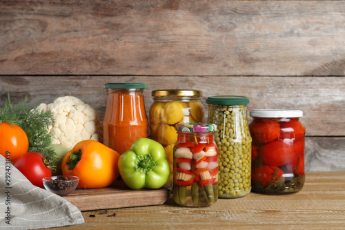 Glass jars with pickled vegetables on wooden table against brown background