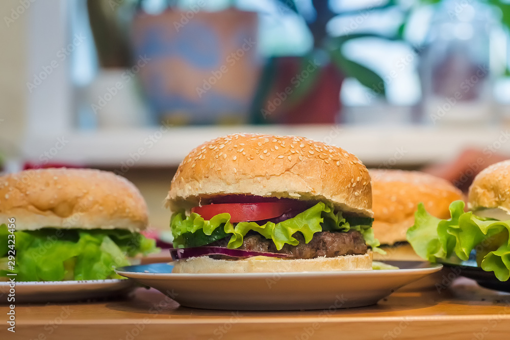 Three Homemade burger with tomato and beef patty, fresh toppings on whole grain artisan bun on kitchen table for dinner Three Homemade burger with tomato and beef patty, fresh toppings on whole grain artisan bun on kitchen table for dinner