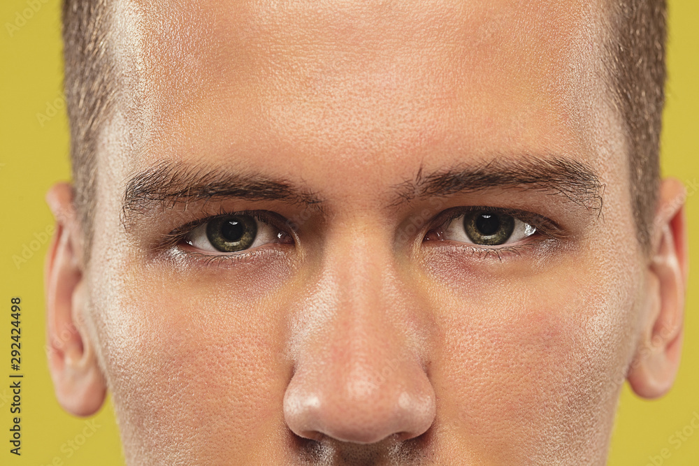 Obraz premium Caucasian young man's close up on yellow studio background. Beautiful male model with well-kept skin. Concept of human emotions, facial expression, sales, ad. Copyspace. Eyes looking at camera.