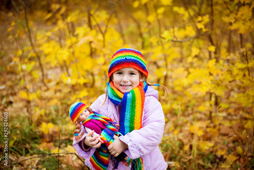 girl in rainbow scarf and hat in autumn dressed the same as a doll