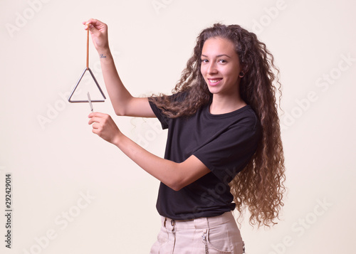Young girl with long curly hair holds a musical triangle in her hand and strikes with the fretboard