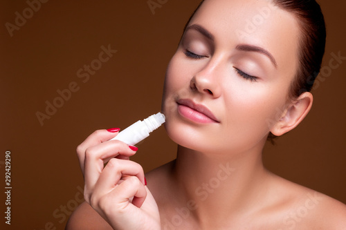 Brunette european woman apply lipstick on her lips on pink neutral background. Flawless clean fresh skin. Beauty process concept