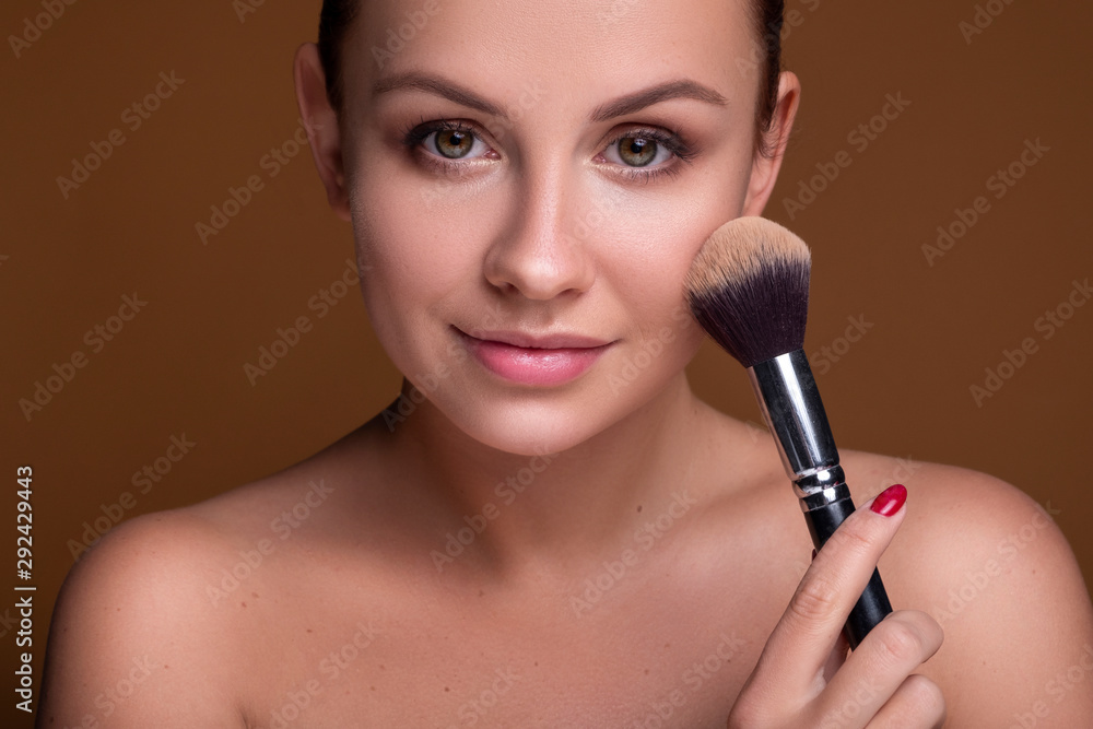 Caucasian brunette woman apply blush on a cheekbone with a brush. Close up portarait. Skin care concept Caucasian brunette woman apply blush on a cheekbone with a brush. Close up portarait. Skin care concept