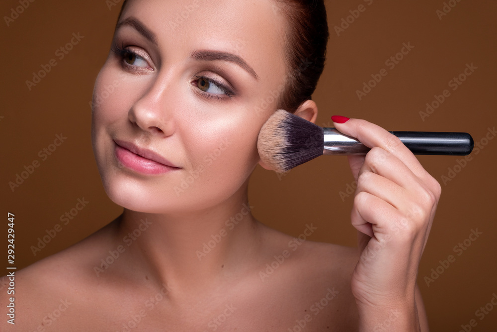 Caucasian brunette woman apply blush on a cheekbone with a brush. Close up portarait. Skin care concept Caucasian brunette woman apply blush on a cheekbone with a brush. Close up portarait. Skin care concept