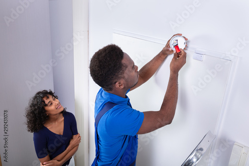 Repairman Changing Battery In Smoke Detector On Wall