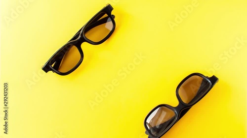 Stop motion animation of view from above of two pair 3D black glasses danсing with each other on yellow background 