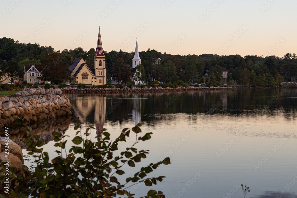 Three churches along the waterfront in Mahone Bay, Nova Scotia, reflected in the water at sunrise on a beautiful morning.