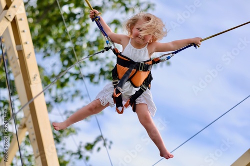Cute girl is jumping on a trampoline with rubber ropes. Extreme activities for children and fun outdoor adventures for a family.